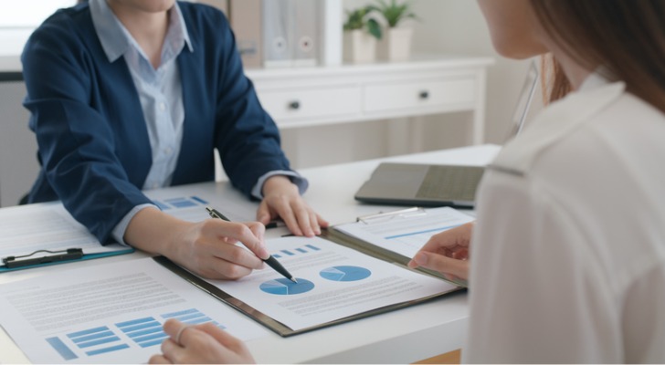 A woman points to graphs while another looks on.